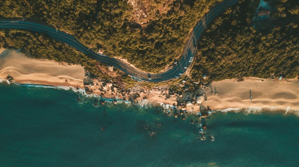 Drone shot capturing lush foliage, winding road, and pristine beach in Balneário Camboriú, Brazil.